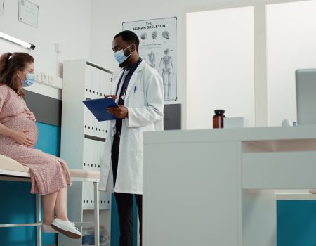 doctor and pregnant woman with face mask attending checkup visit
